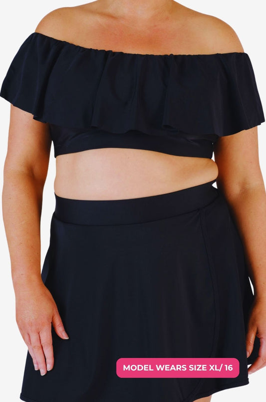 Black off-shoulder swim top and high-waisted swim skirt worn by a model size XL/16 set on a grey background