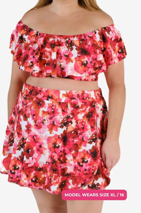 Model size XL/16 wearing a floral off-shoulder swim top and high-waisted swim skirt set on a grey background