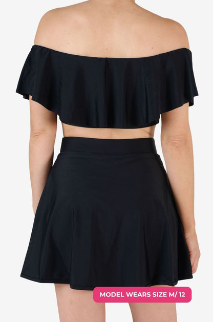 Back view of a black off-shoulder swim top and high-waisted swim skirt worn by a model size M/12 set on a grey background