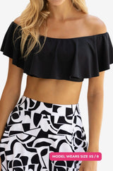 Close up of a black off-shoulder swim top worn by a model size XS/8 set on a grey background