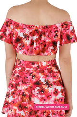 Back view of a model size M/12 wearing a floral off-shoulder swim top and high-waisted swim skirt set on a grey background