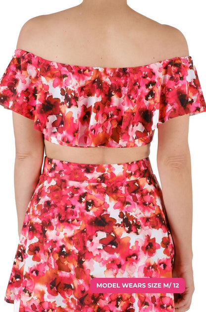 Back view of a model size M/12 wearing a floral off-shoulder swim top and high-waisted swim skirt set on a grey background