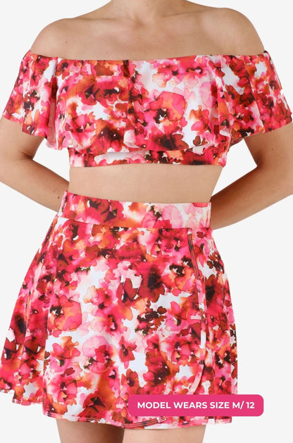 Close up of a model size M/12 wearing a floral off-shoulder swim top and high-waisted swim skirt set on a grey background