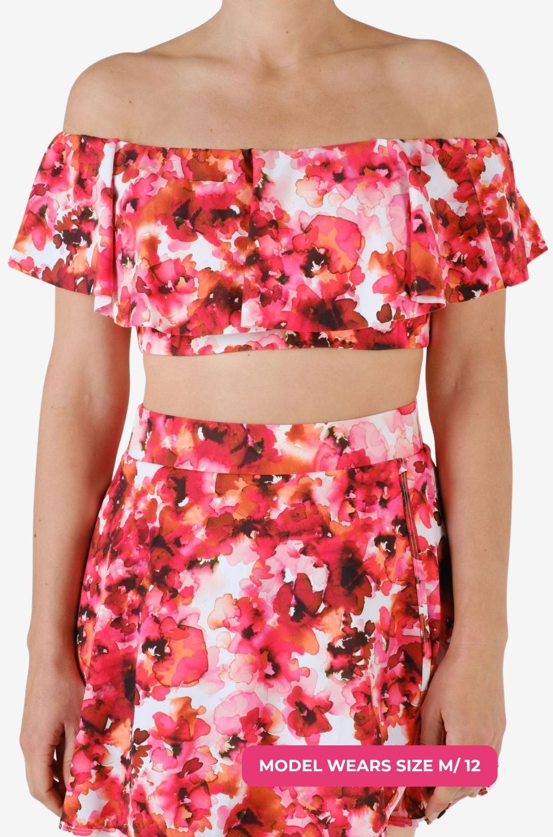 Model size M/12 wearing a floral off-shoulder swim top and high-waisted swim skirt set on a grey background