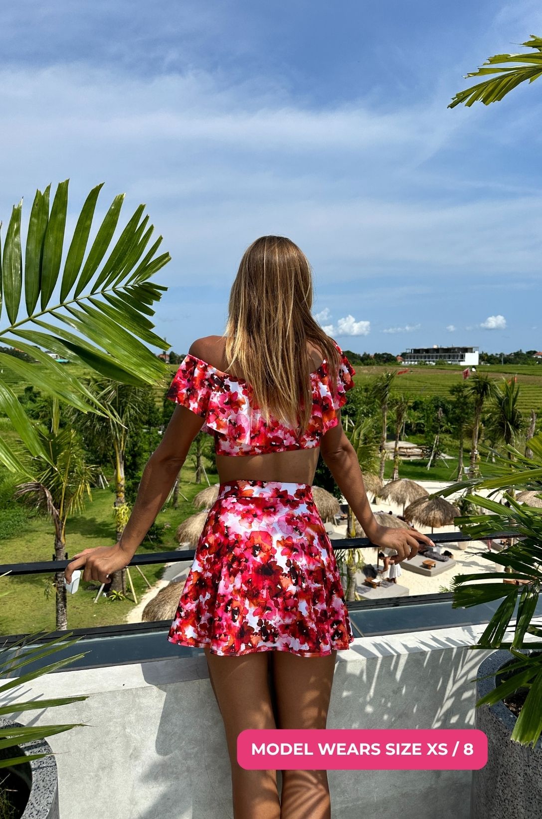 Model size XS/8 wearing a floral off-shoulder swim top and high-waisted swim skirt overlooking tropical fields