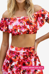 Close up of a model size XS/8 wearing a floral off-shoulder swim top and high-waisted swim skirt set on a grey background