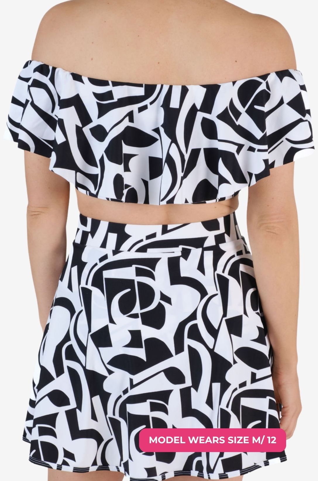 Back view of a black and white geometric patterned off-shoulder swim top and matching high-waisted swim skirt worn on a model size M/12
