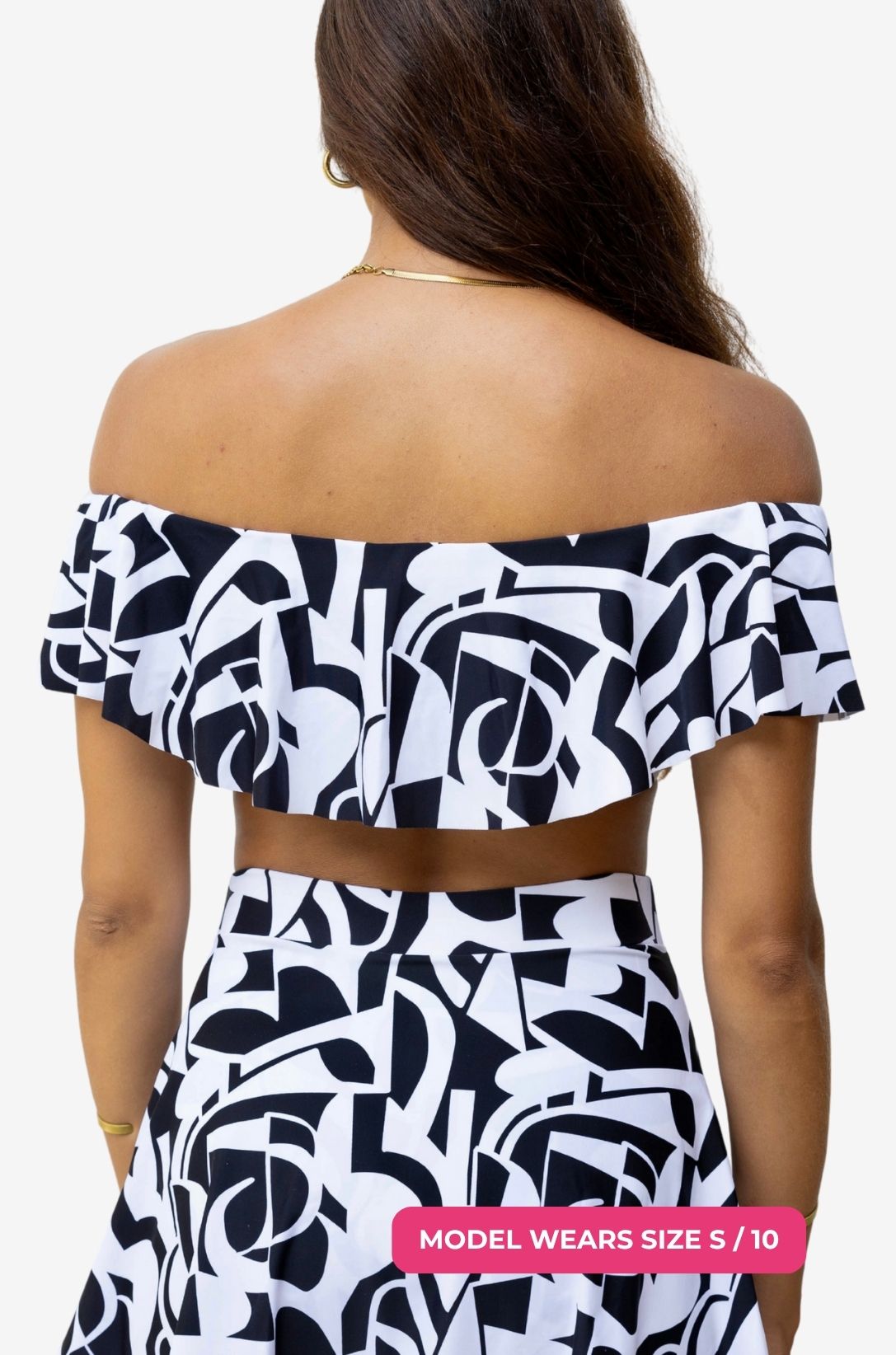 Back view of a black and white geometric patterned off-shoulder swim top worn on a model size S/10