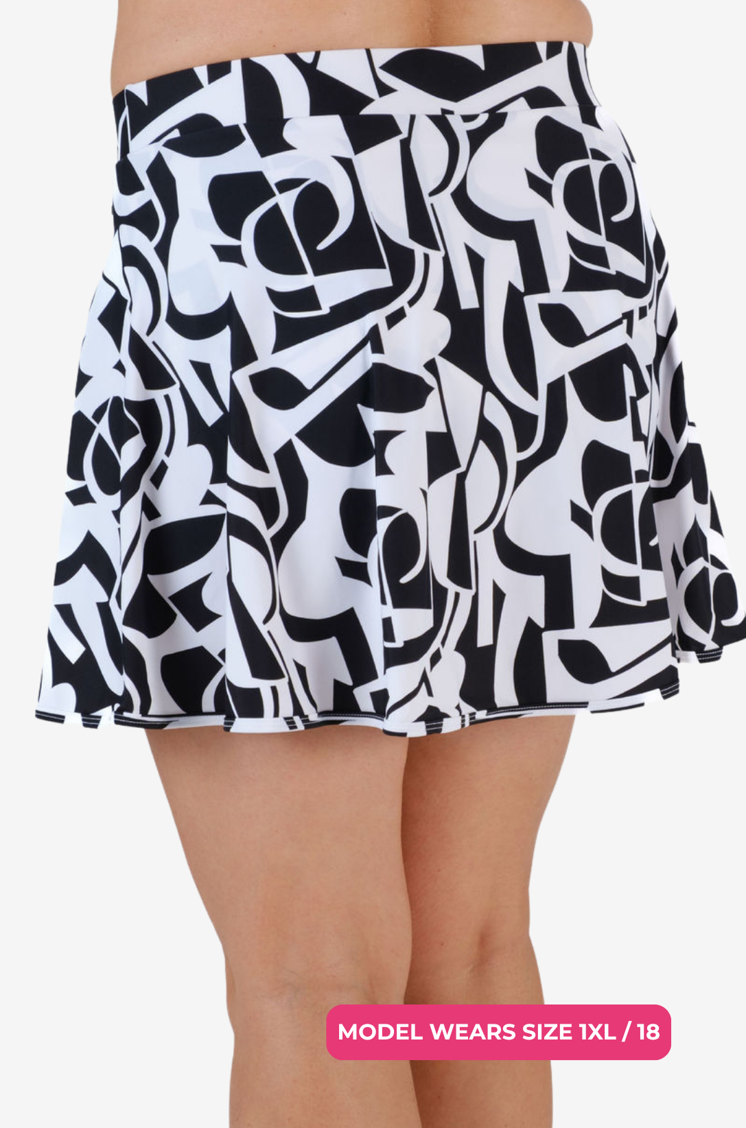 Side view of a model size 1XL/18 wearing a black and white geometric high-waisted swim skirt on a grey background