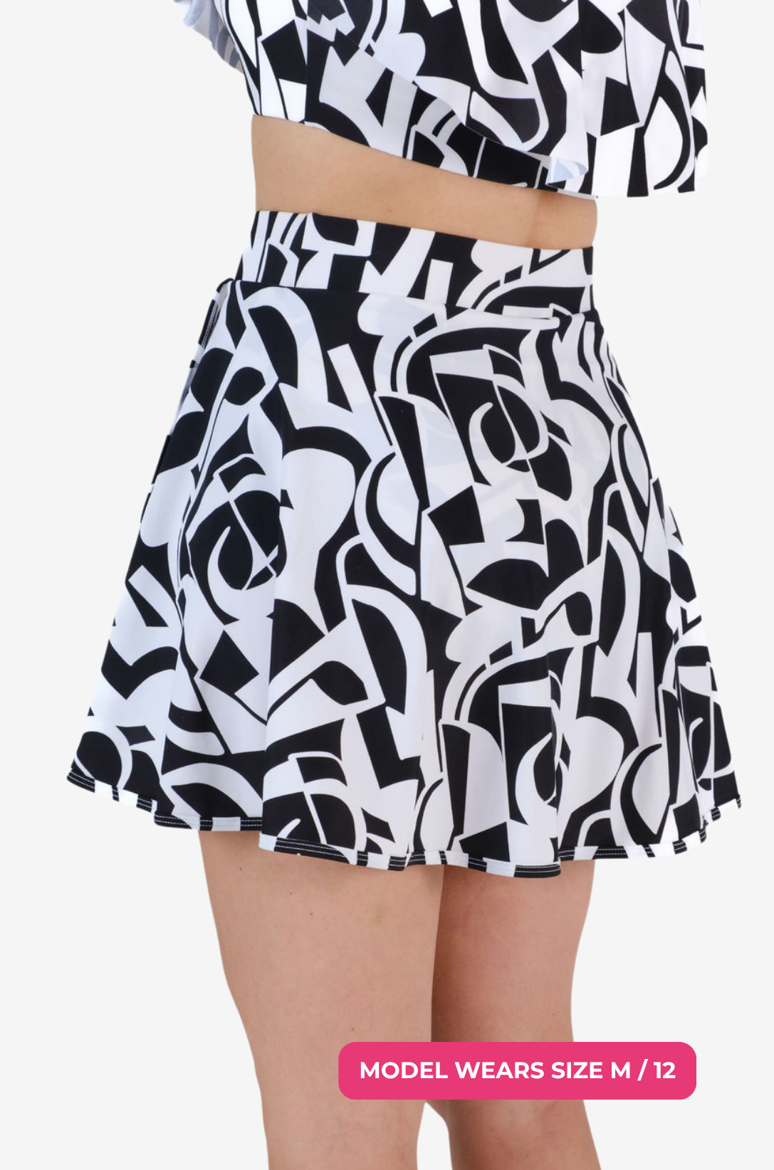 Side back view of a model size M/12 wearing a black and white geometric high-waisted swim skirt on a grey background