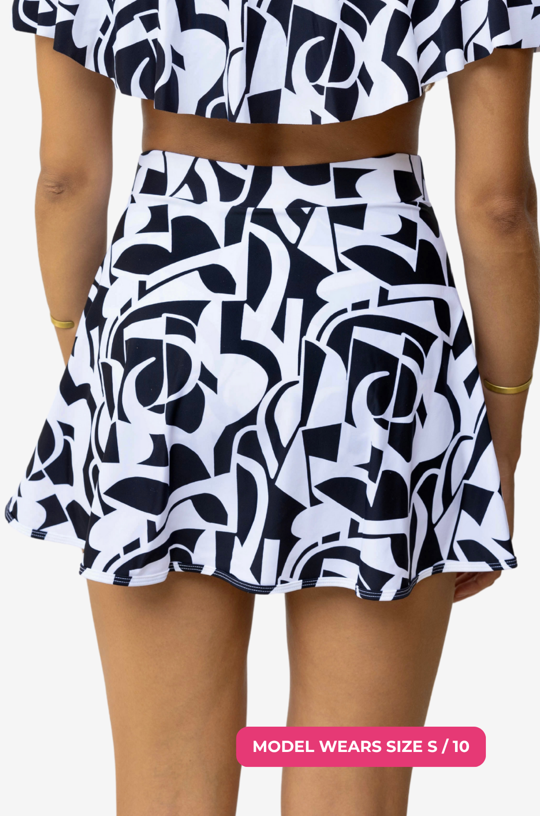Back view of a model size S/10 wearing a black and white geometric high-waisted swim skirt on a grey background